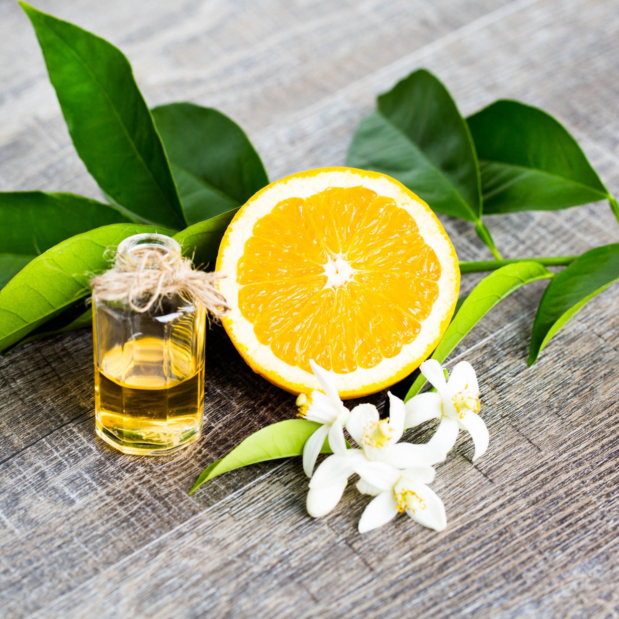 Orange slice with green leaves and a small glass bottle on a wooden surface