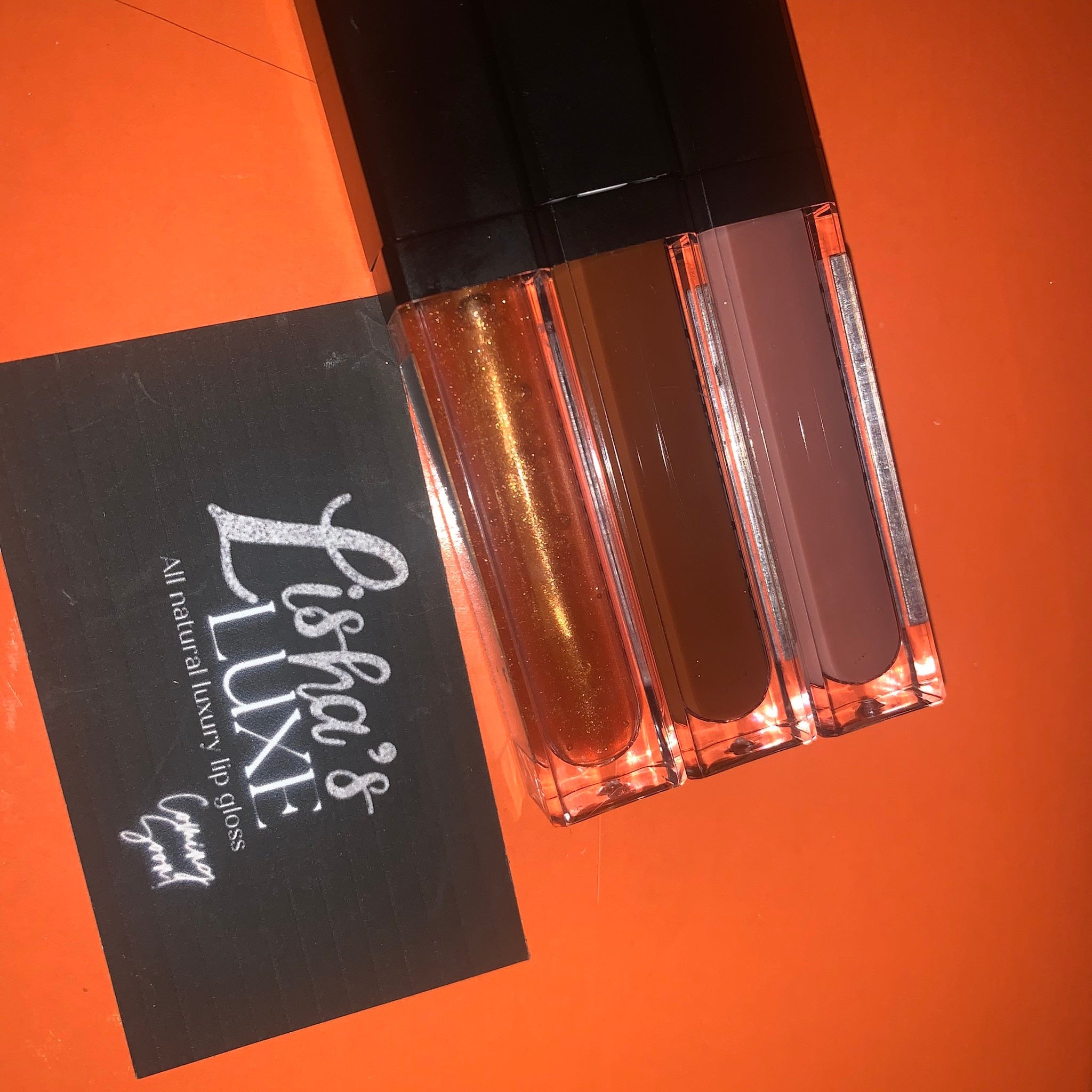 Lip gloss tubes with clear, brown, and mauve colors, LishasLuxe brand visible on black card