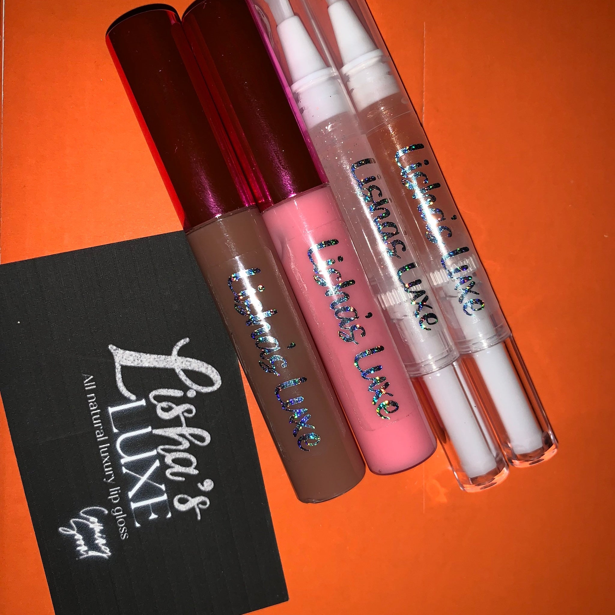 Lip gloss tubes with brown, pink, and clear colors, Lishas Luxe branding, on orange background