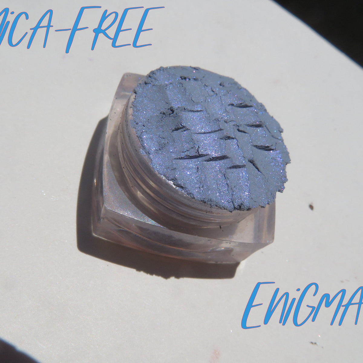 Close-up of Enigma Blue Shimmer loose mineral eyeshadow with reflective particles in glass jar
