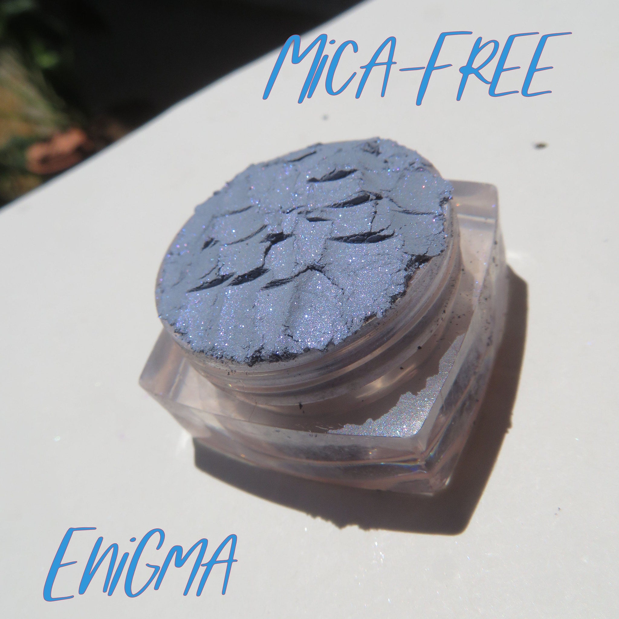 Close-up of Enigma Blue loose mineral eyeshadow with shimmer particles, showcasing vibrant teal hue and fine powder texture.