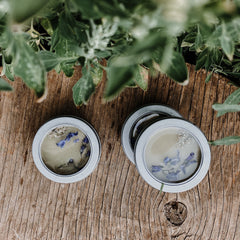 Skin care salve in silver tins with blue flowers on wood surface