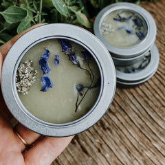 Candle with blue and white floral accents in silver tin, held in hand