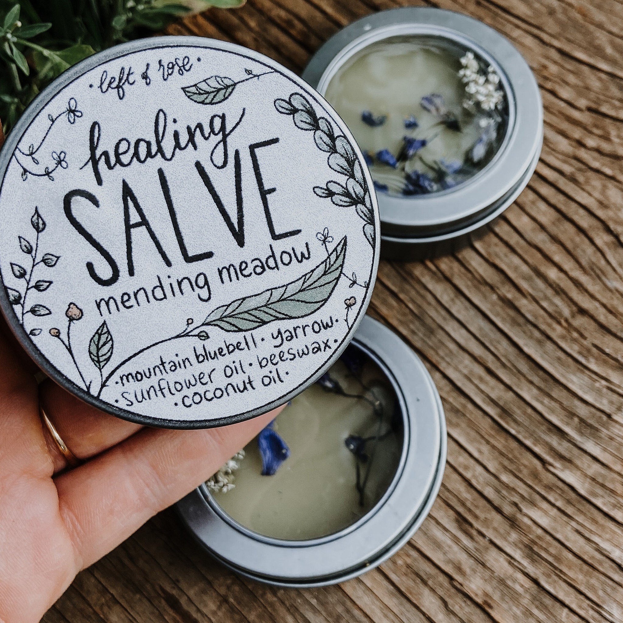 Healing salve tin with floral design, black text, and silver tin on wood surface.