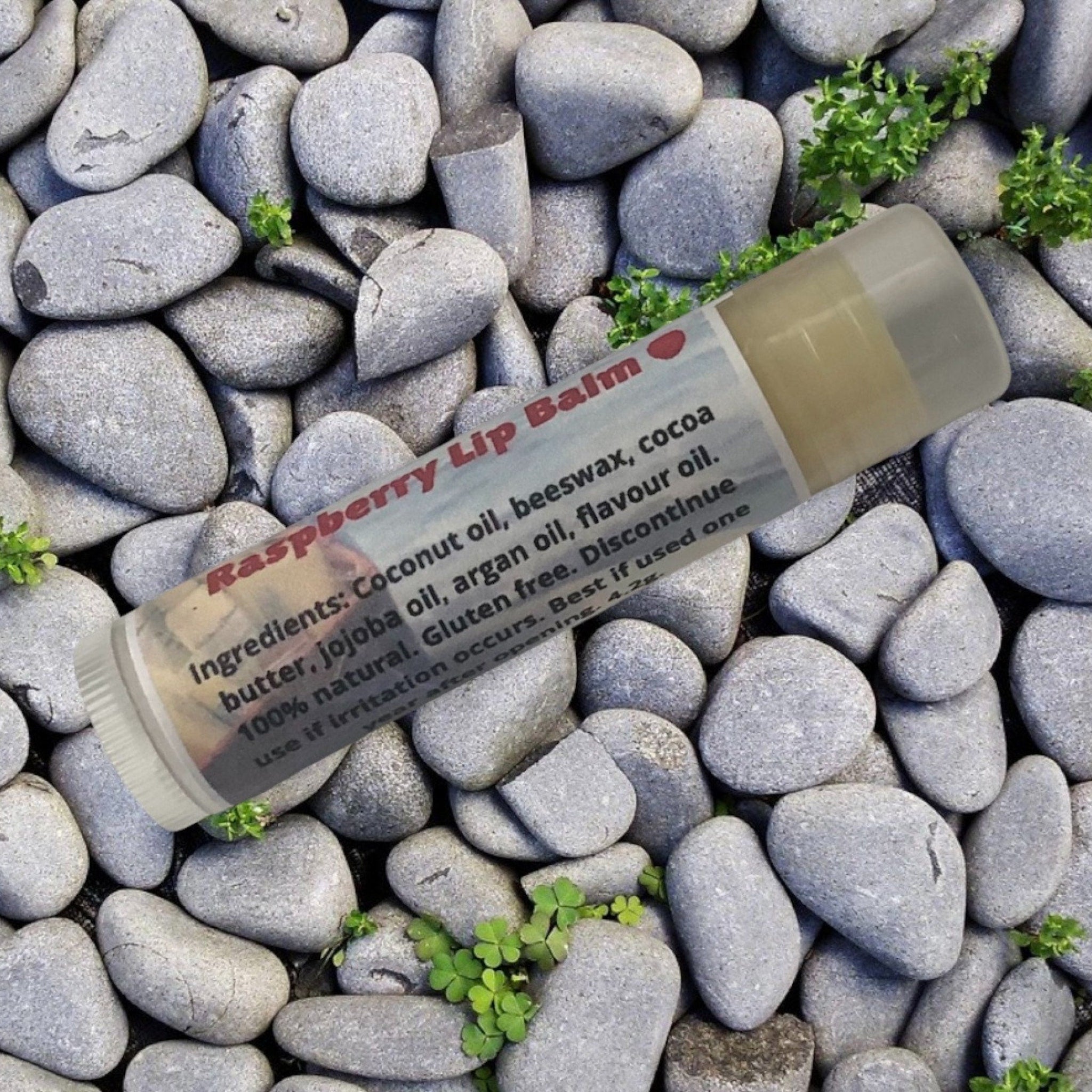 Lip balm tube with white and clear casing, raspberry label, on gray rocks