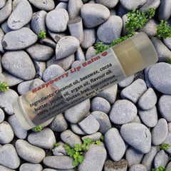 Lip balm tube with white and clear casing, raspberry label, on gray rocks