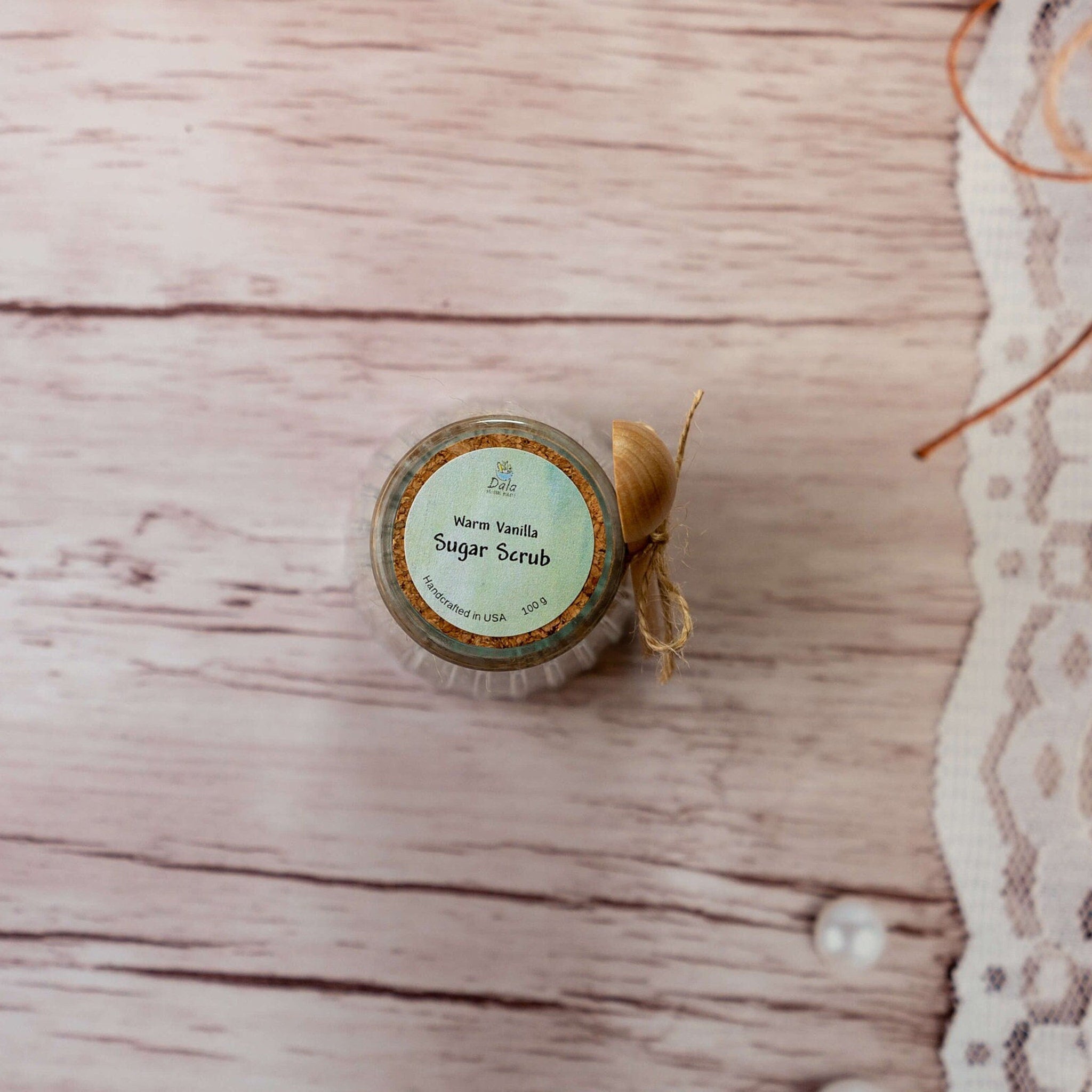 Sugar scrub jar with cork lid, paper label, and twine bow on wood background