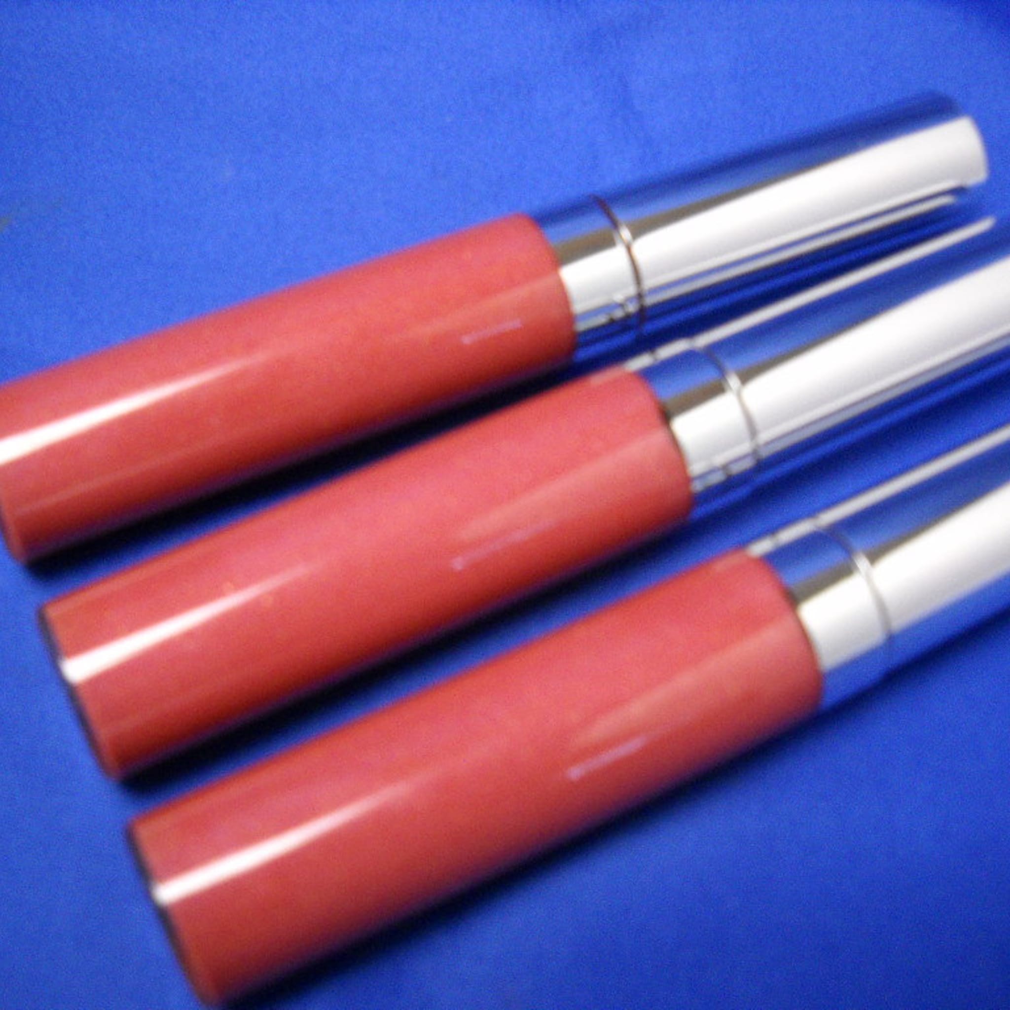 Lip gloss tubes with red bodies and silver caps on blue background
