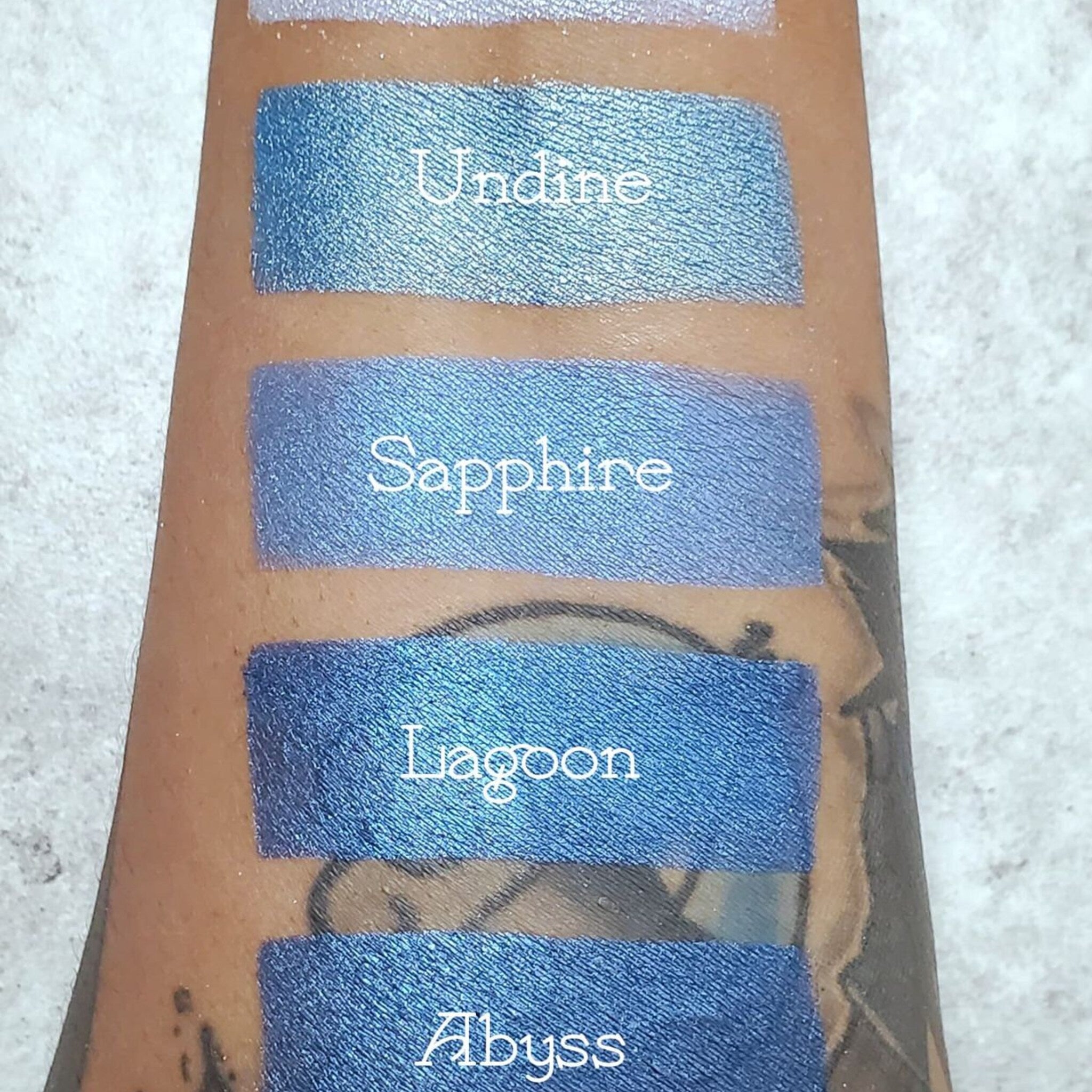 Square sapphire blue eyeshadow compact with vegan label, displayed open on marble surface