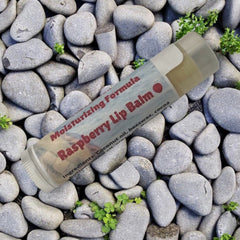 Raspberry Lip Balm in a clear tube with gray label and red text, on gray stones