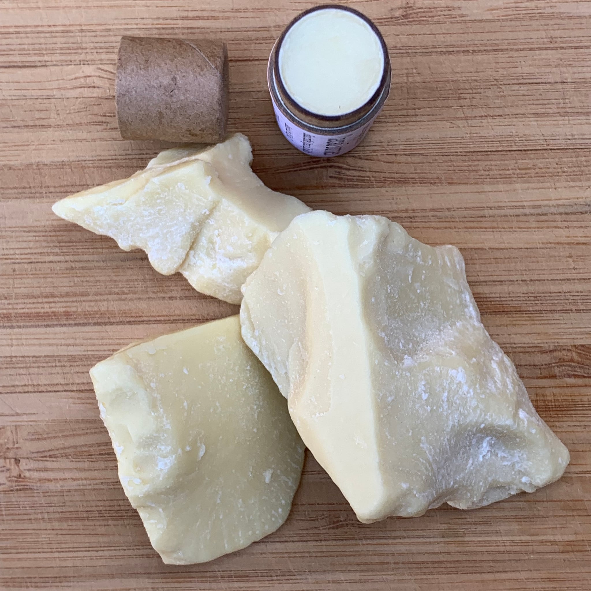 Cocoa butter chunks, off-white pieces, brown roll, small jar with cream on wood surface