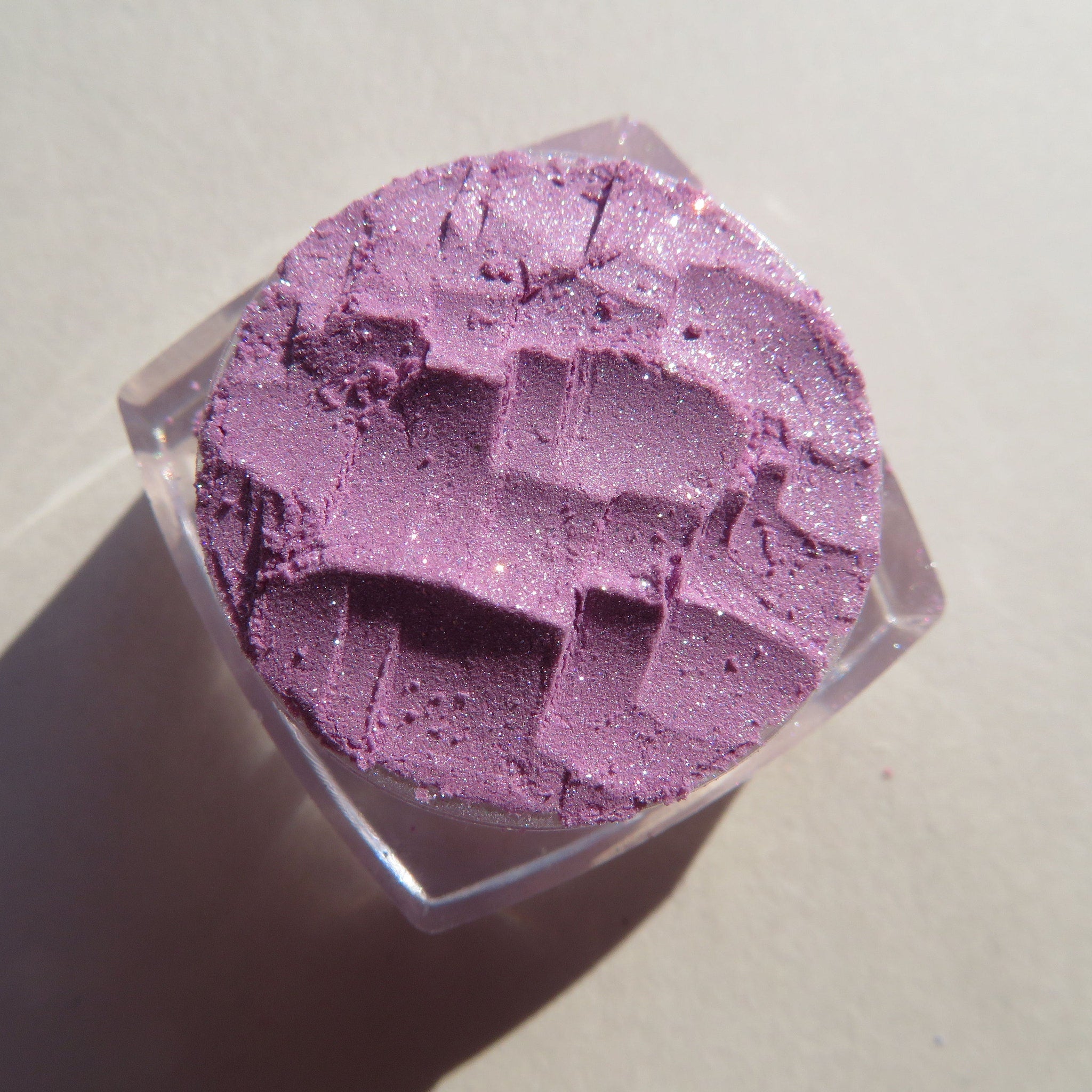 Eyeshadow powder in purple with glitter and textured pattern in clear container