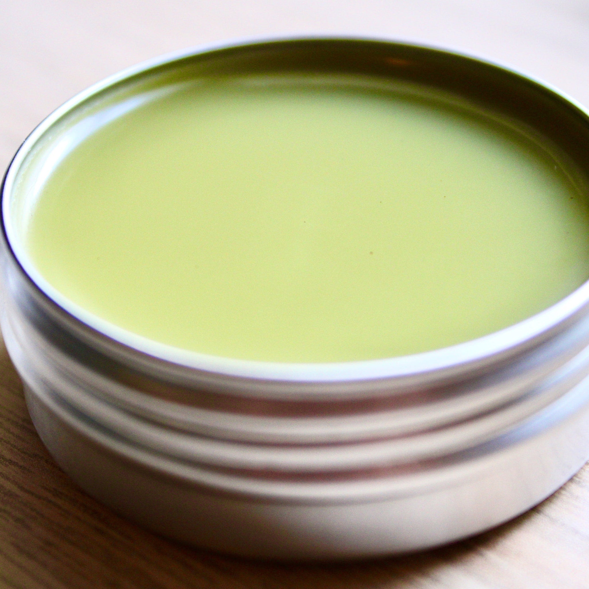 Green balm in silver tin, smooth pale green color, metallic container, on wood surface