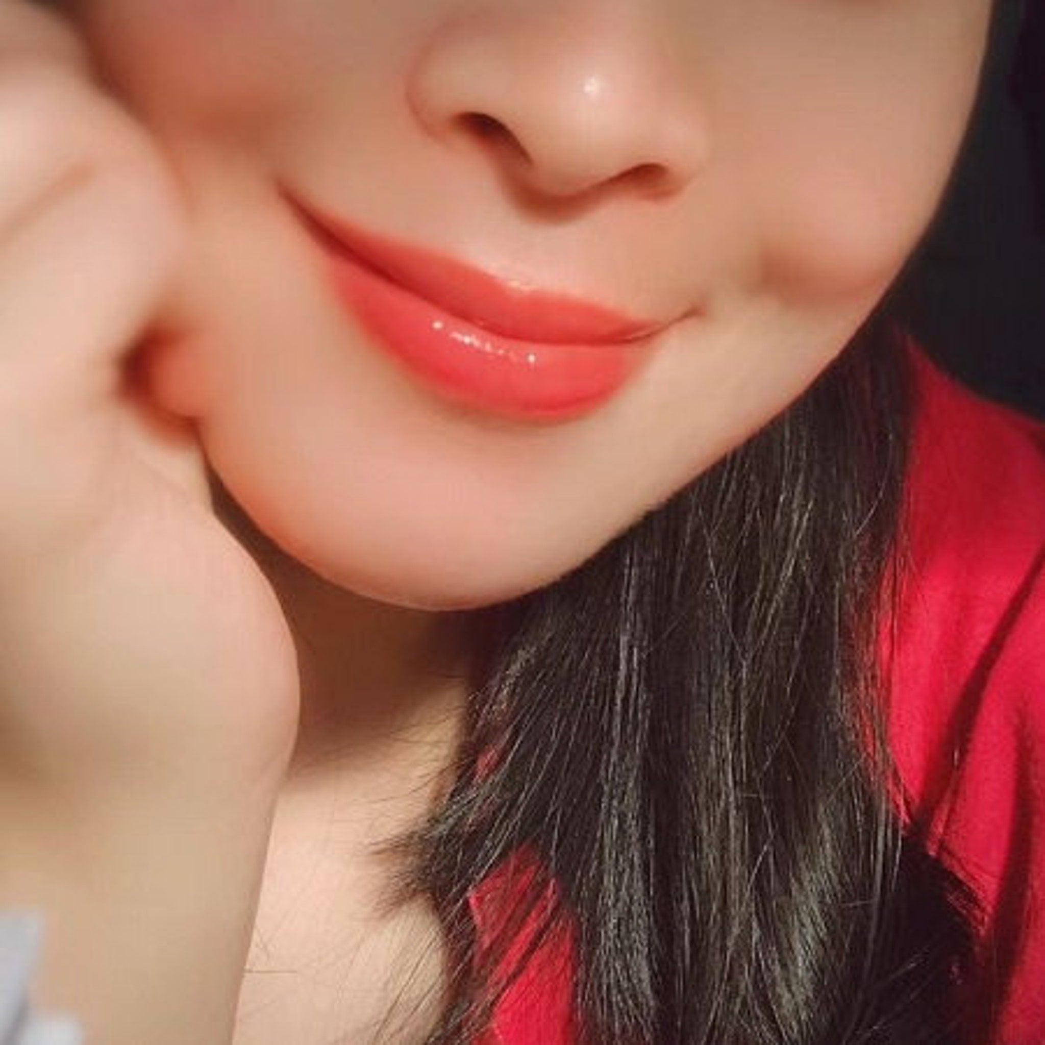 Lip gloss in coral color with glossy finish, shown on smiling face with red top