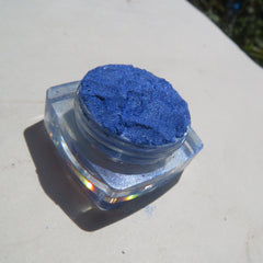 Side view of bright blue shimmer loose mineral eyeshadow in clear jar with silver lid, showcasing pigment texture