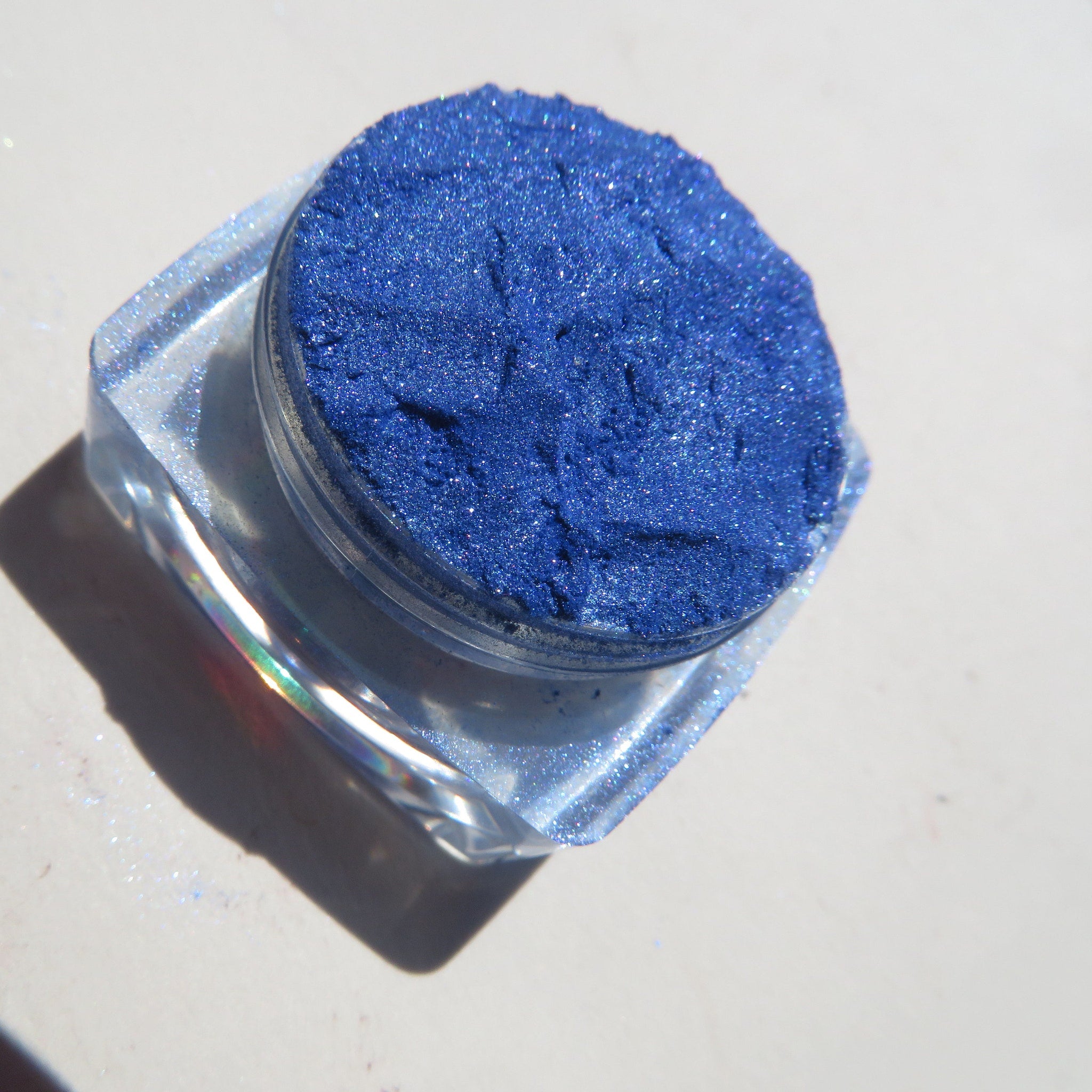 Open jar of bright blue shimmer mineral eyeshadow with loose pigment and vegan label visible