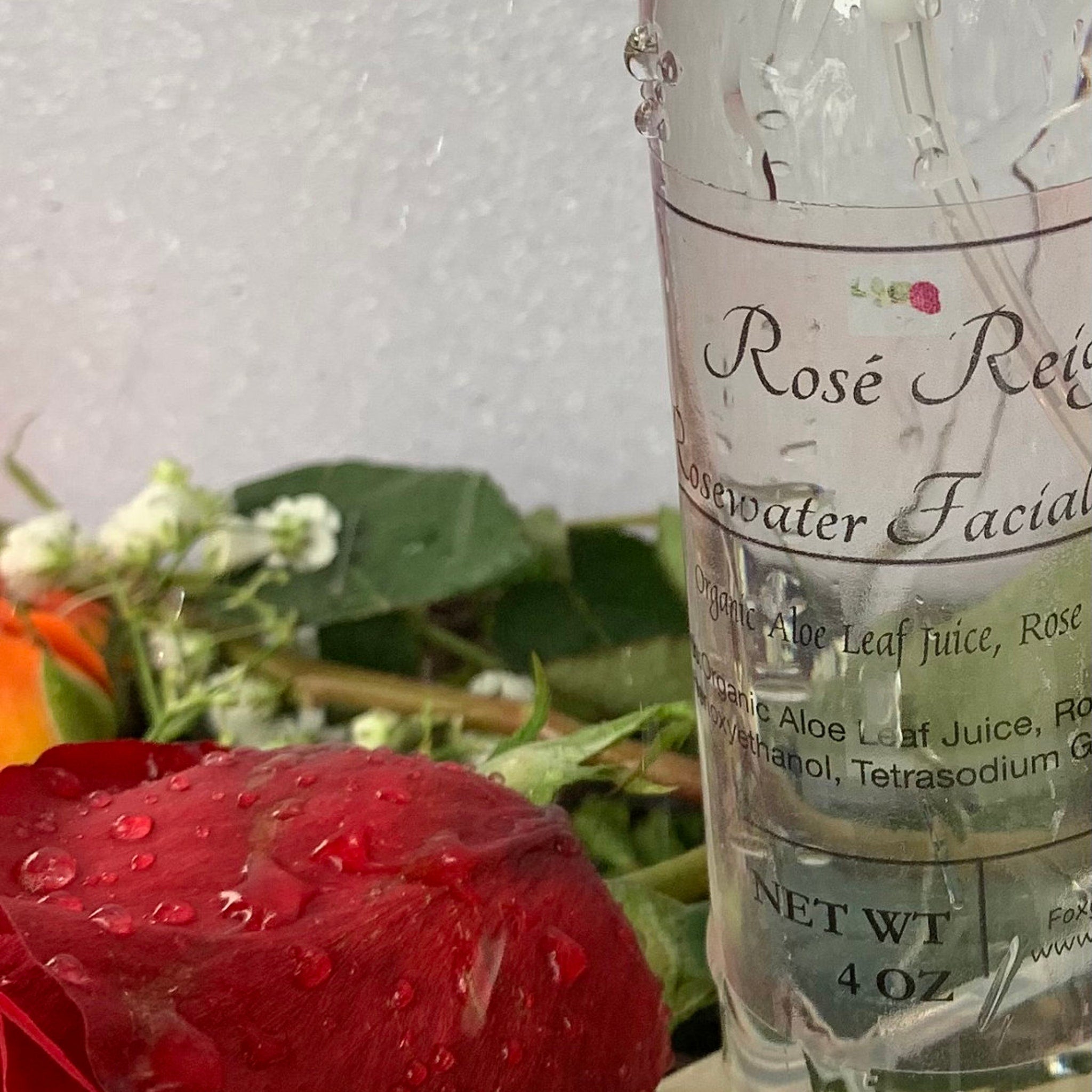 Rosewater Facial, clear glass bottle with label, red rose, and water droplets on surface