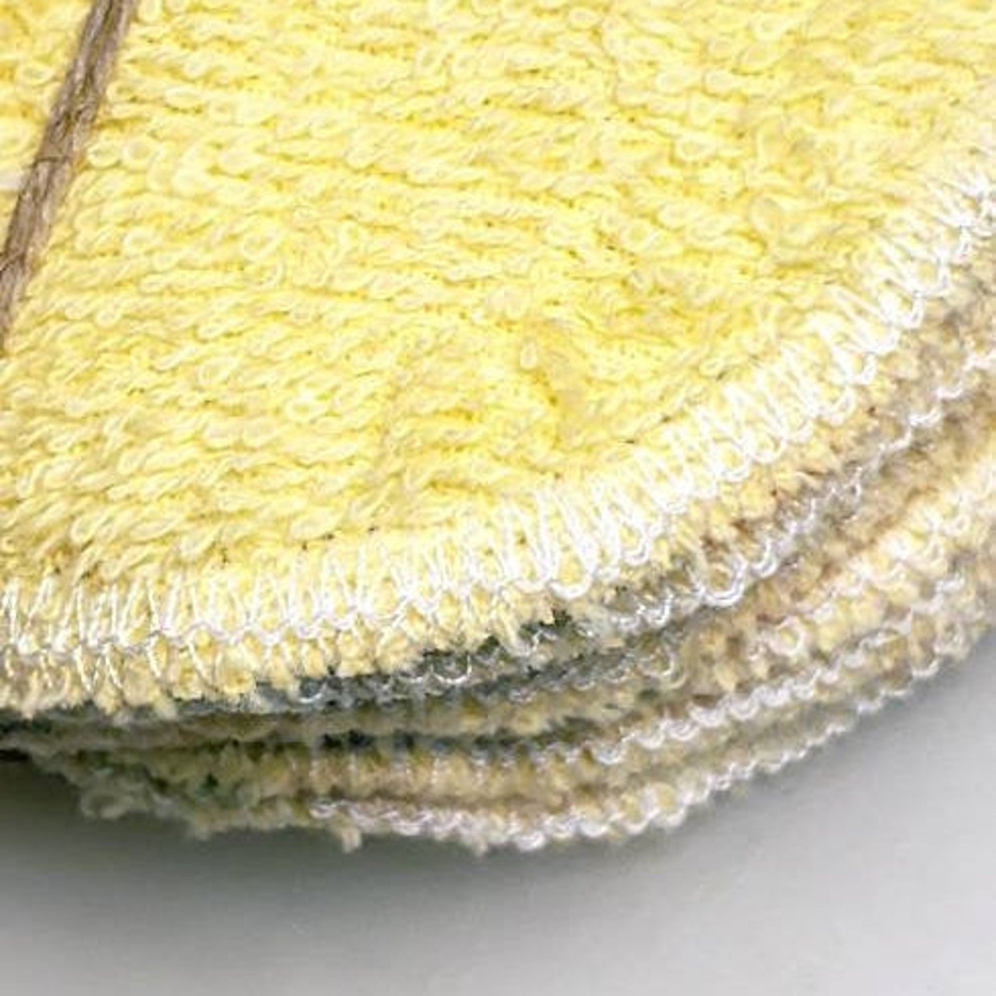 Reusable facial rounds in yellow terry cloth with white stitching and stacked appearance