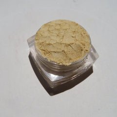 Side view of bright yellow matte loose mineral eyeshadow in a clear jar with black lid, showcasing fine pigment texture.