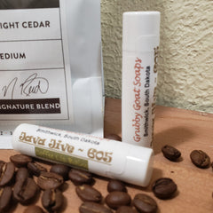 Lip balm with white tube, brown text, and coffee beans on wood surface