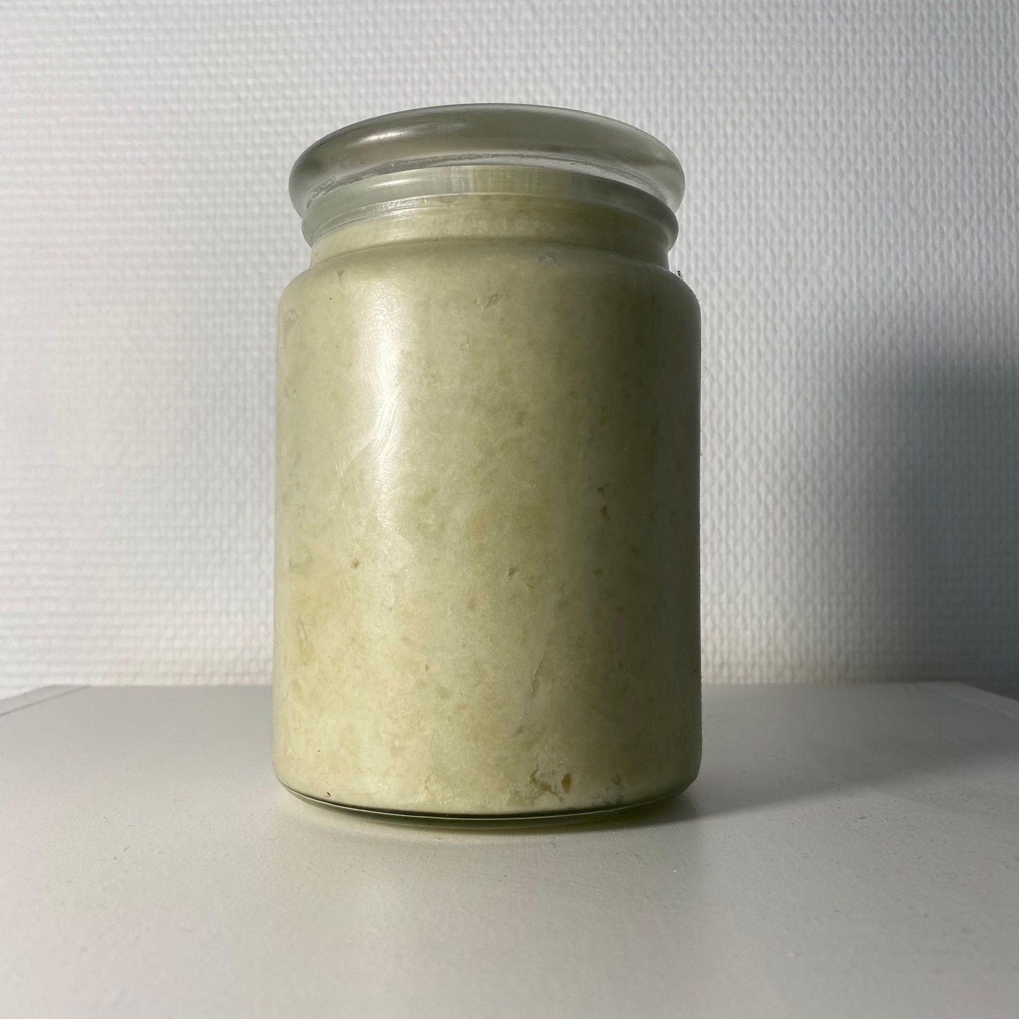 Jar of pale yellow substance in a clear glass jar with a glass lid, sitting on a white surface
