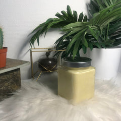 Yellow jar with silver lid on white fluffy surface with green plants in background