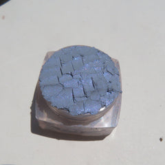 Close-up of loose Enigma Blue Shimmer mineral eyeshadow with reflective particles in vegan, cruelty-free packaging