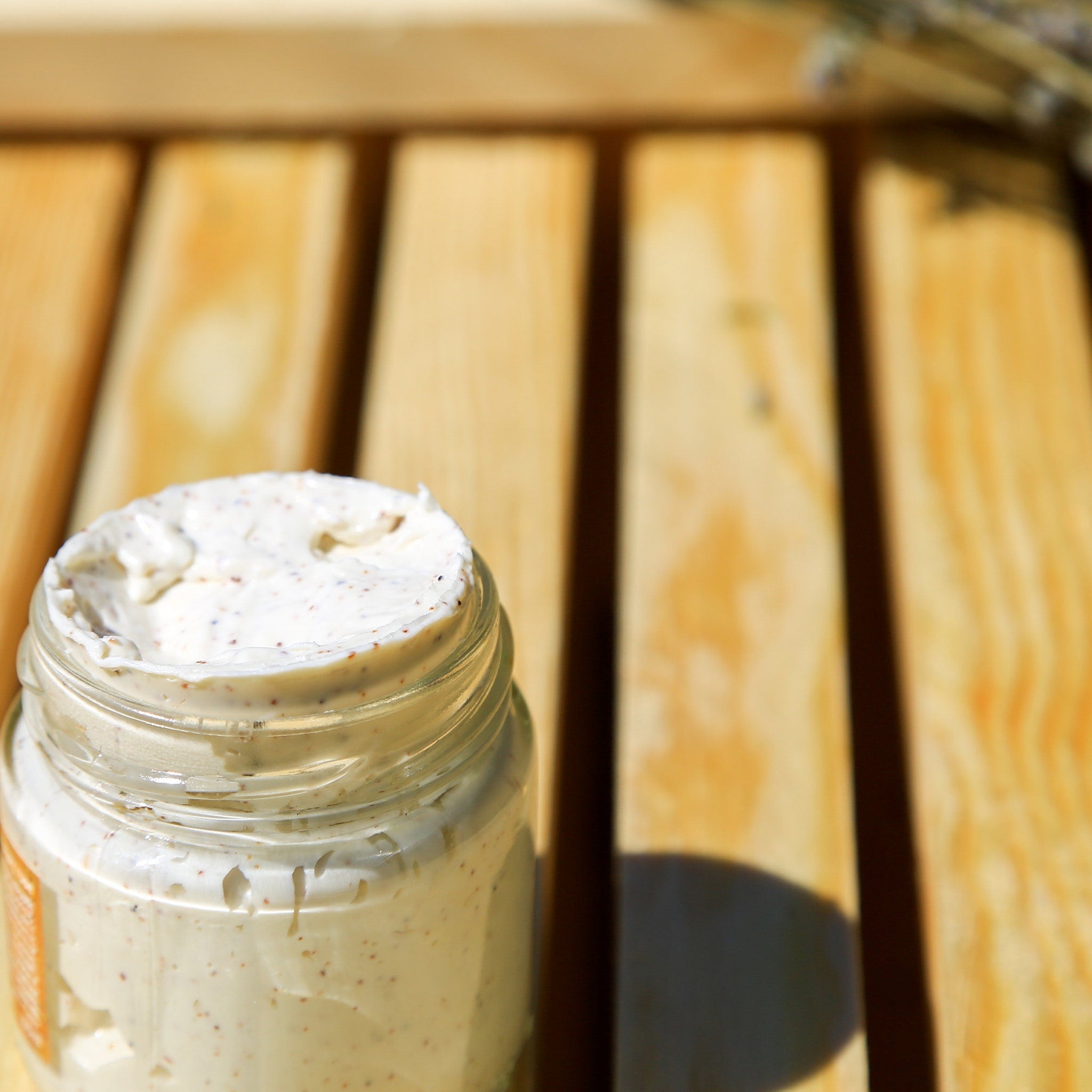 Creamy skincare product in a clear glass jar, with a light beige color and speckled texture, on a wooden surface