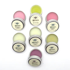Lip balms with various colors in metal tins, Natura Emporium brand name visible