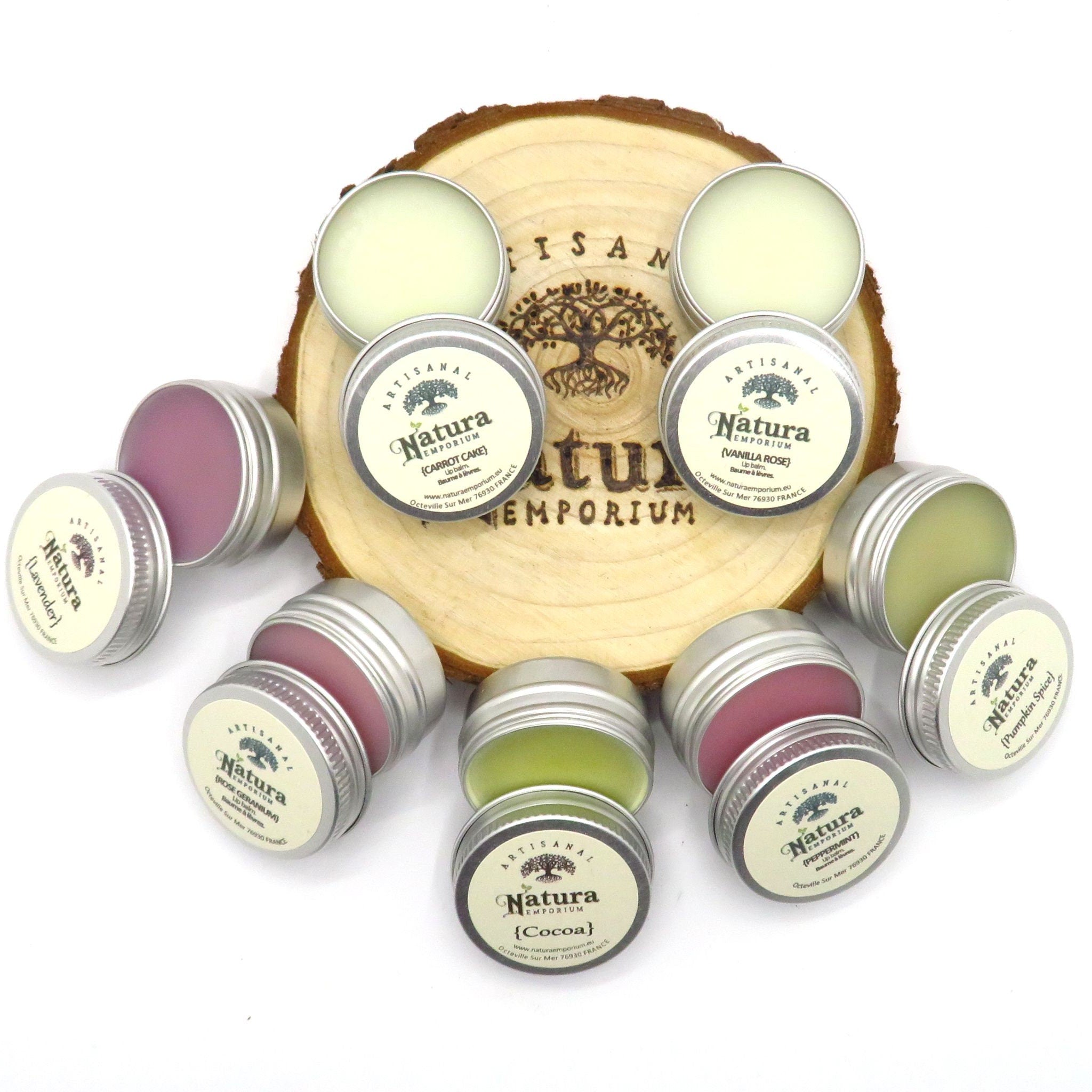 Lip balms in silver tins with Natura Emporium branding, various colors on wooden base