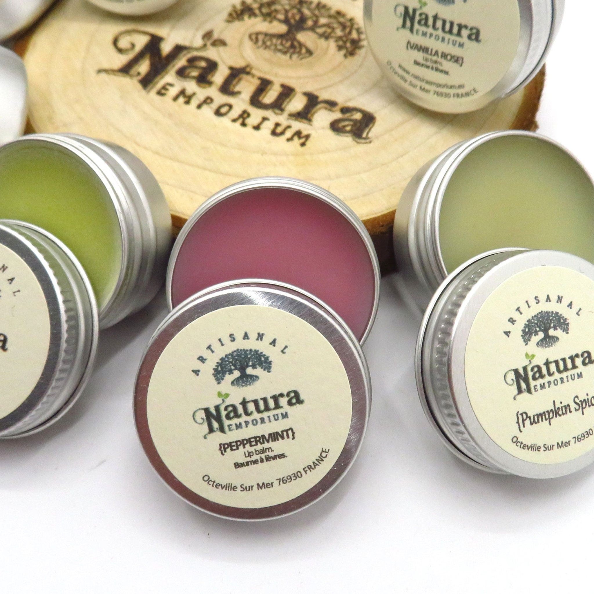 Lip balms in silver tins, with Natura Emporium labels, and various colors visible