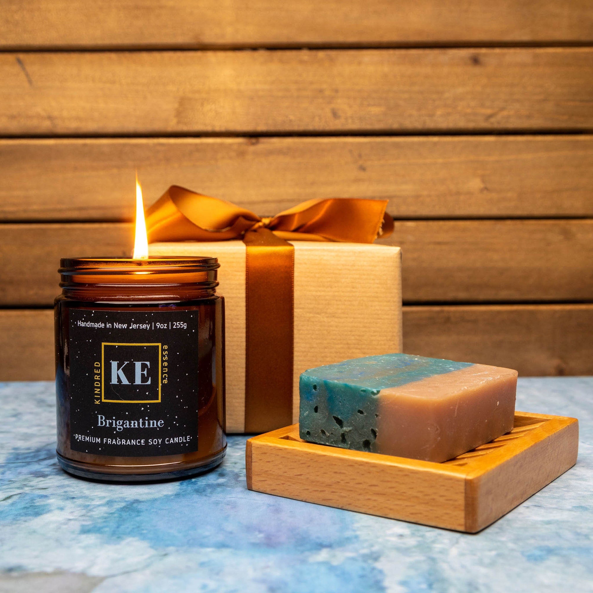 Soy candle in glass jar with lit flame, soap bar and gift box with ribbon