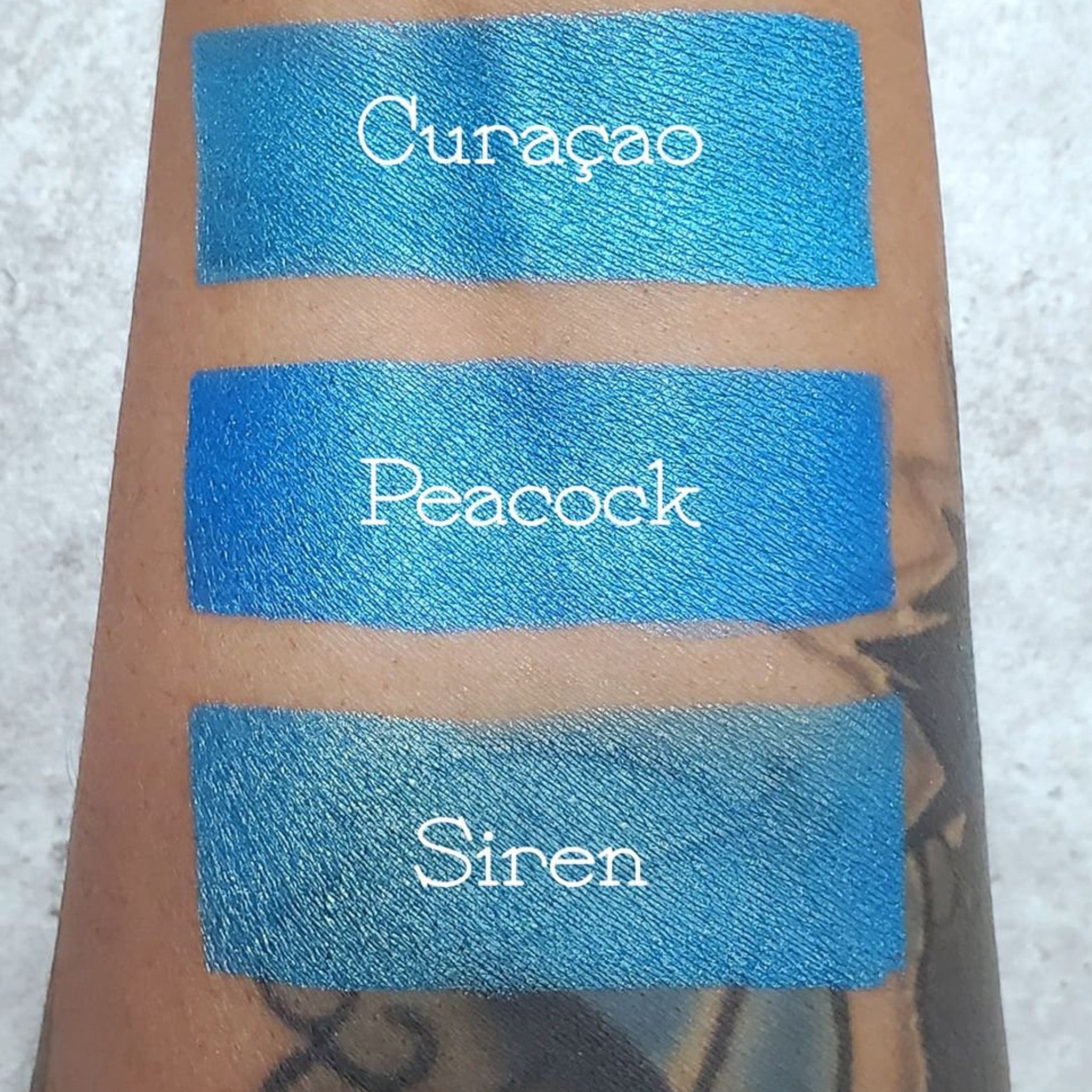 Close-up of teal blue vegan eyeshadow pan showing smooth pressed powder texture and rich pigment saturation