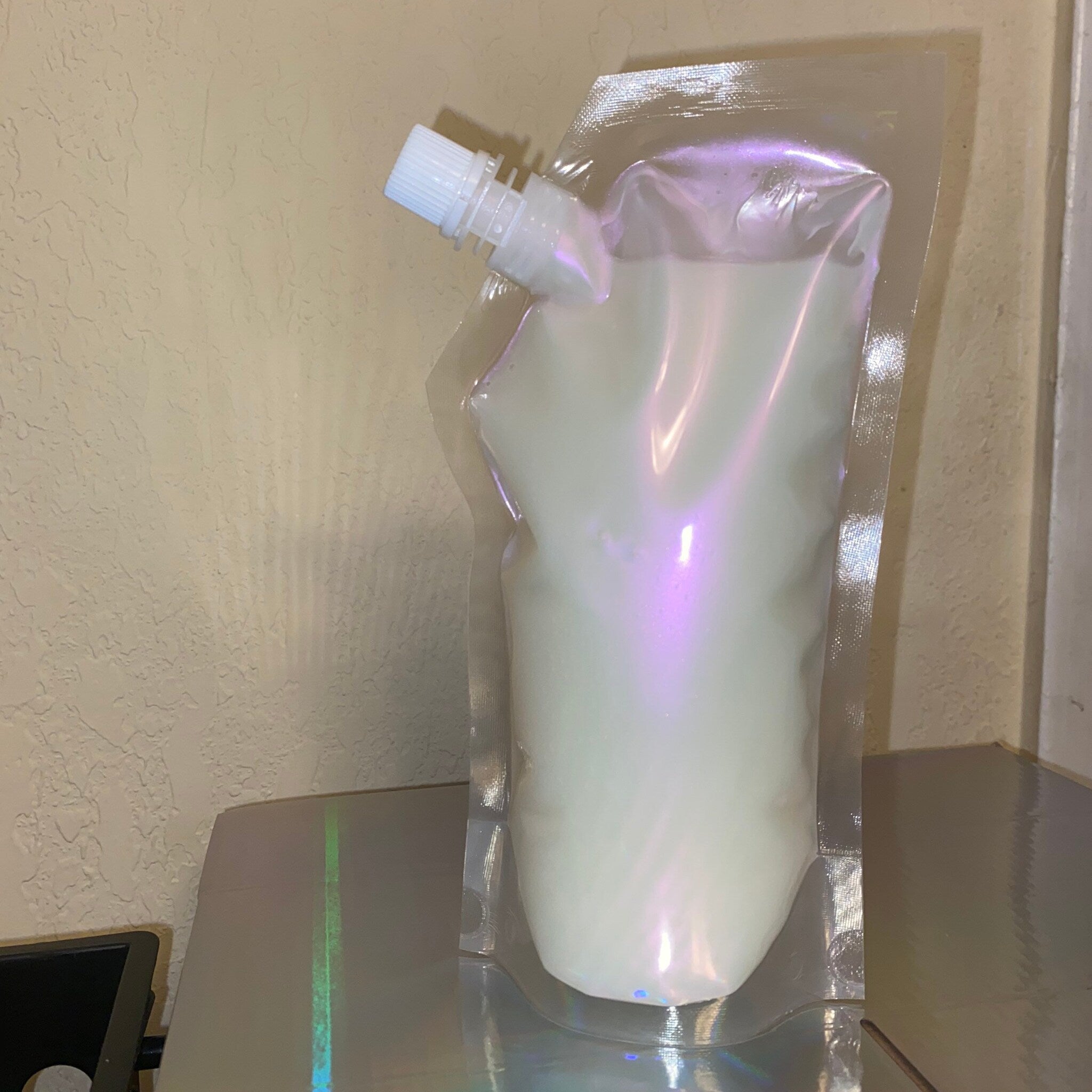 Clear plastic pouch with white liquid, iridescent sheen, and white spout for dispensing