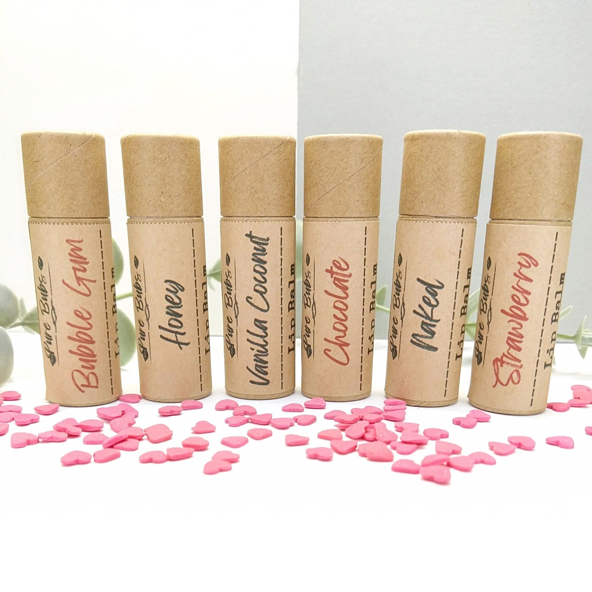 Lip balms in brown cardboard tubes with flavor labels, Pure Bubs brand, and pink heart confetti