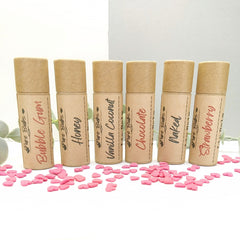 Lip balms in brown paper tubes with flavor labels, pink heart sprinkles around them