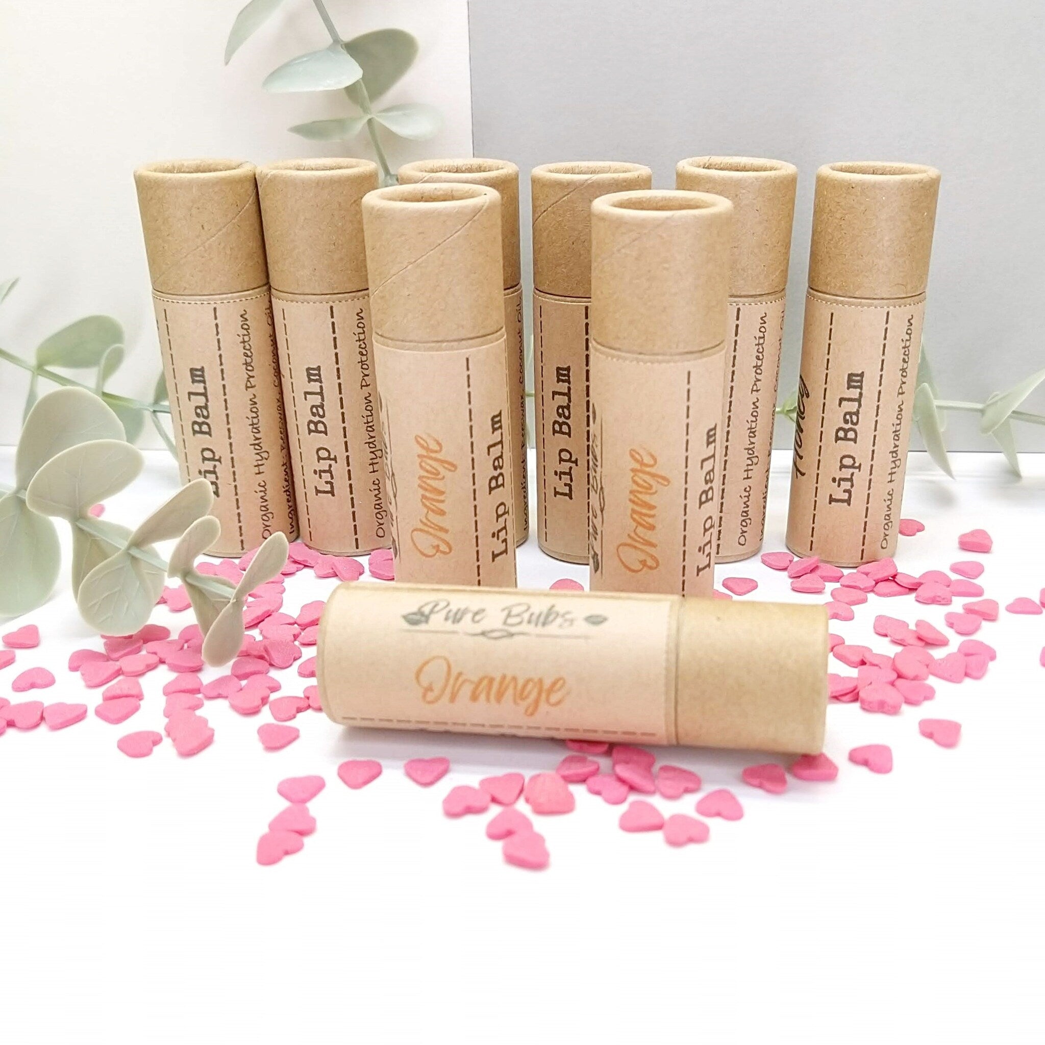 Lip balm tubes in brown paper, with "Orange" text, and pink heart confetti