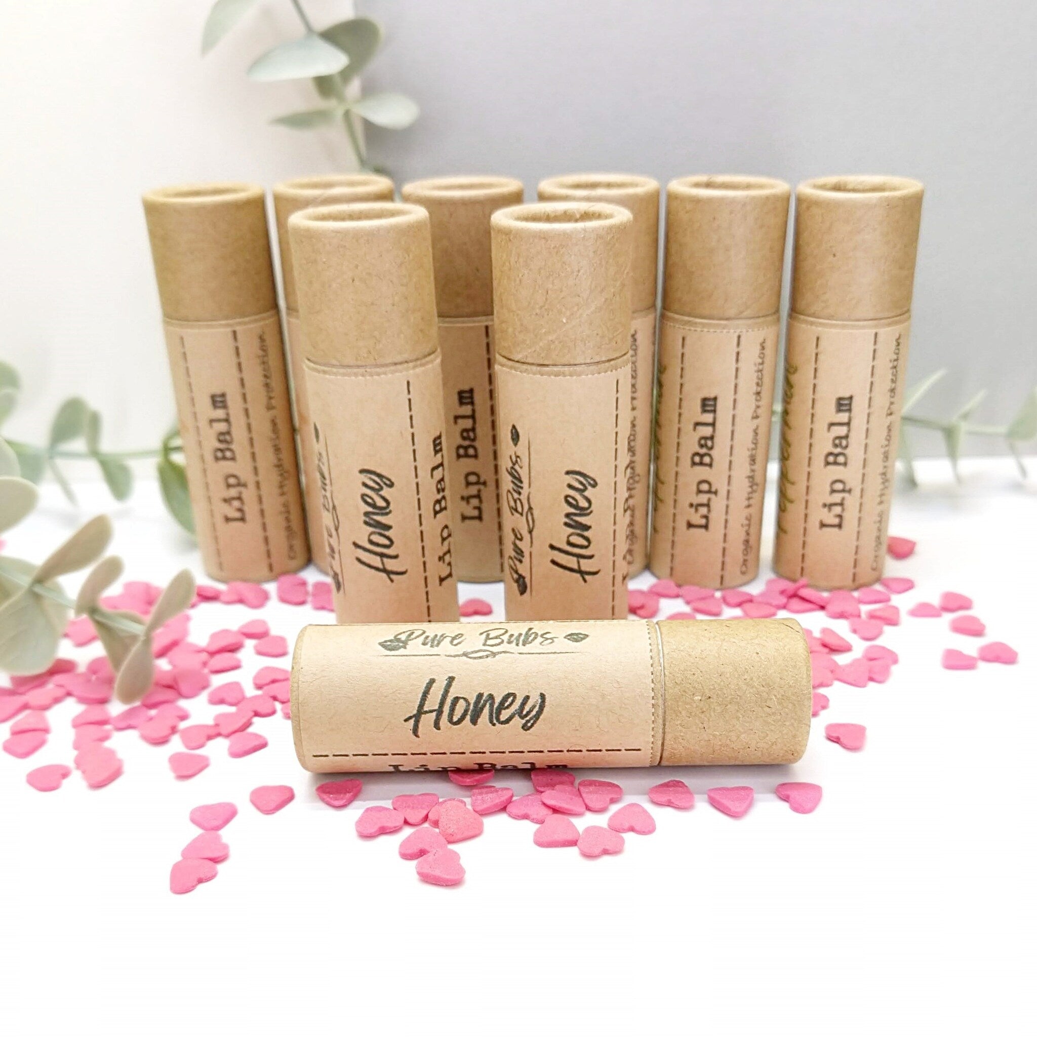 Lip balm tubes in brown cardboard with "Honey" label and pink heart confetti