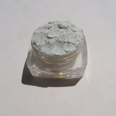 Close-up of matte pale green loose mineral eyeshadow with fine powdery texture in eco-friendly packaging