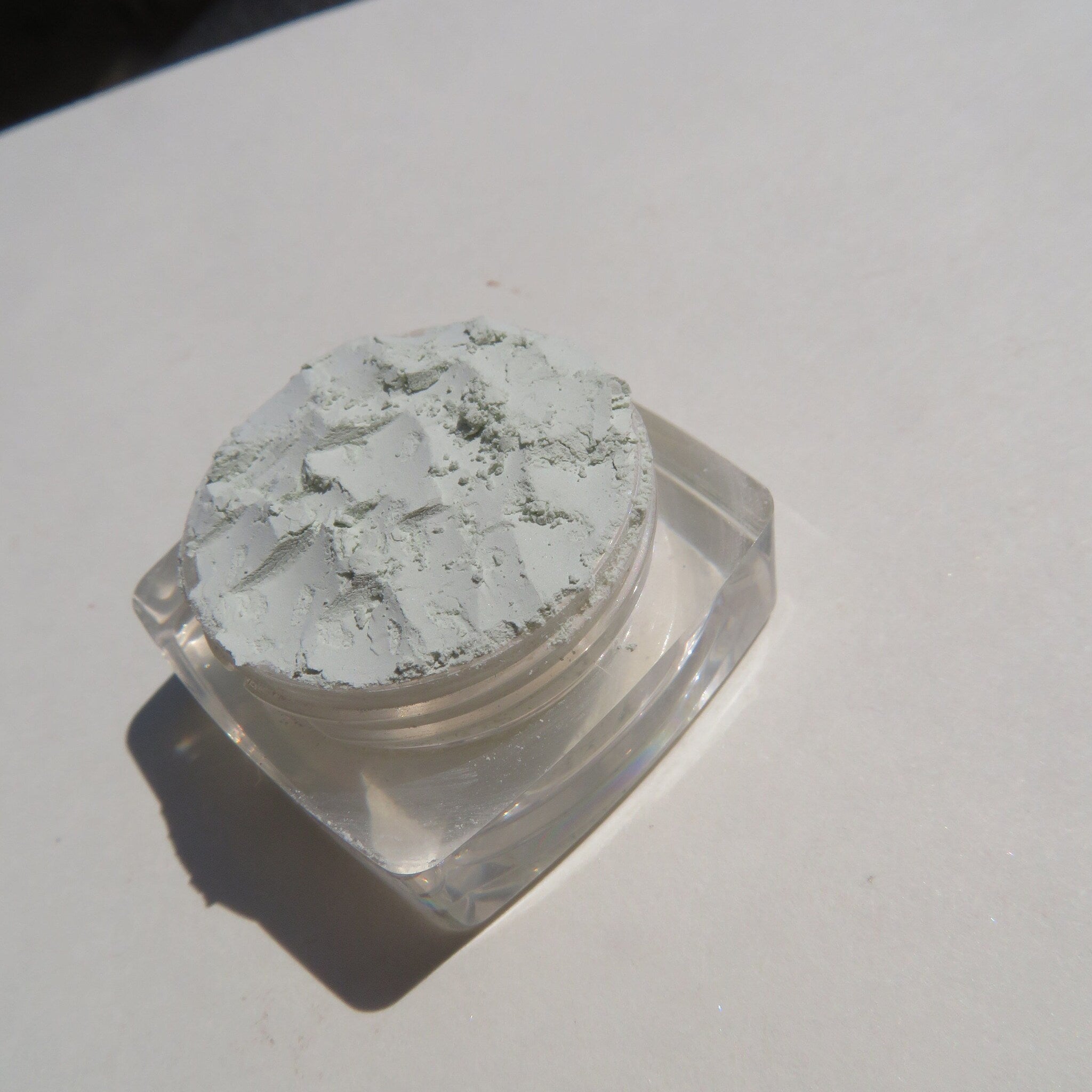 Pale green mineral eyeshadow jar with matte finish and eco-friendly label on wooden surface