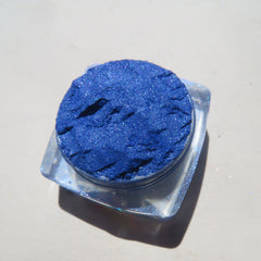 Hand applying bright blue shimmer mineral eyeshadow with fingertip onto eyelid, showcasing loose pigment texture