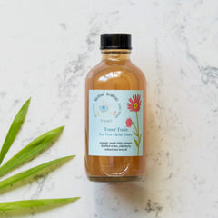 Tea Tree Toner in glass bottle with black cap, Ballerina Botanicals label, on marble surface