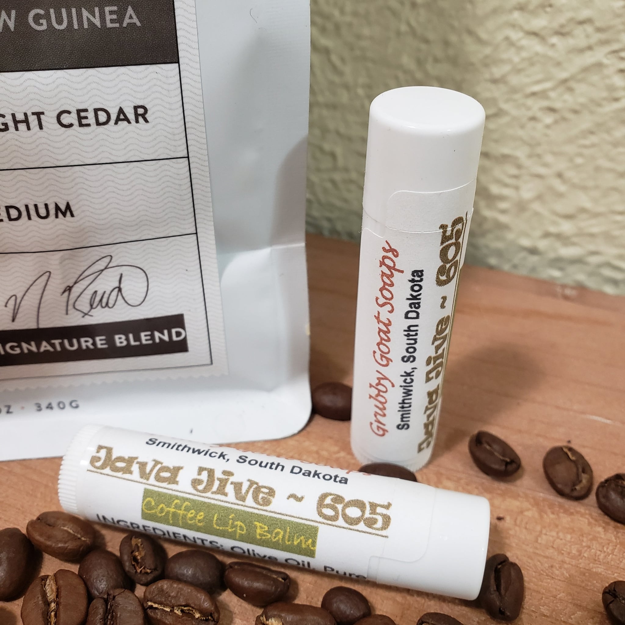 Lip balm tubes with white and gold text, coffee beans on wood surface, Grubby Goat Soaps brand