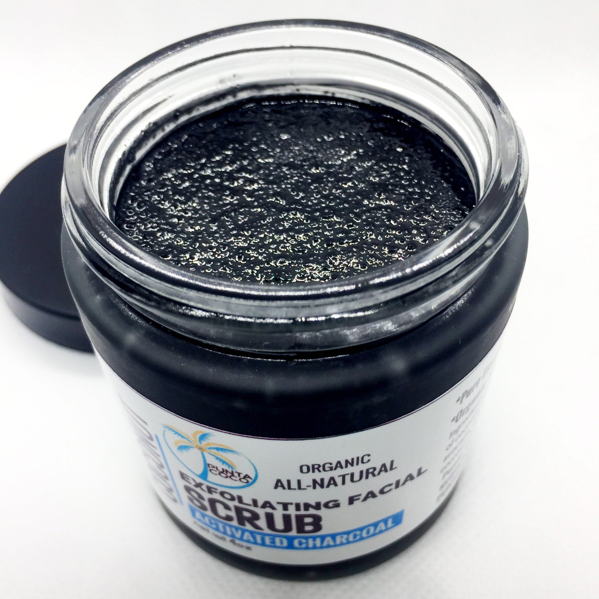 Activated charcoal exfoliating facial scrub in a black jar with a clear glass rim and a black lid, Punta Coco brand