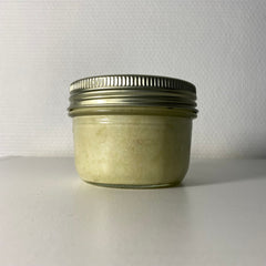 Jar of cream with glass and metal lid, light yellow color, on white surface.