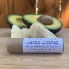 Lip balm tube with Sweet Poppy Homestead label, brown paper, and avocado slices on wood surface