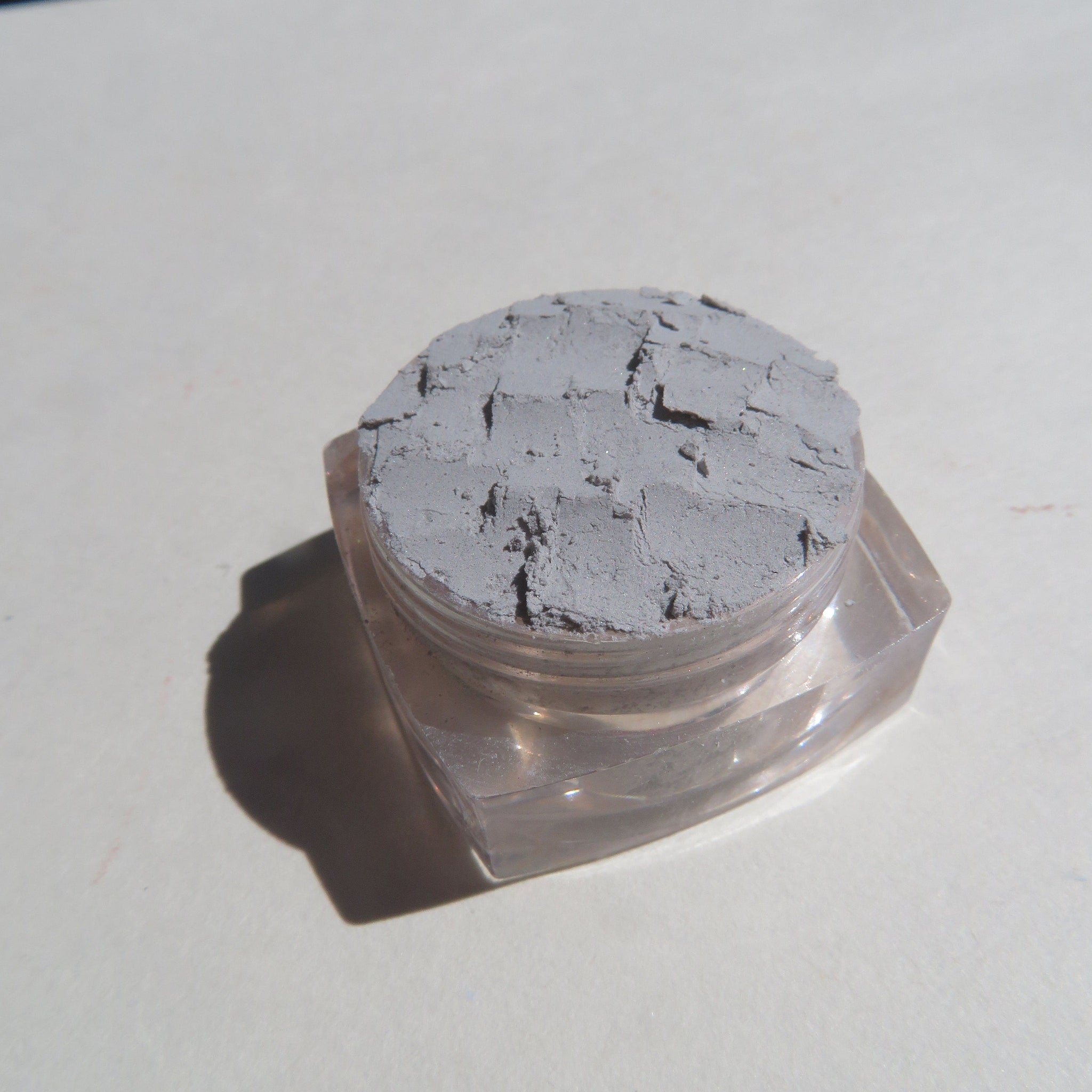 Close-up of pale matte gray mineral eyeshadow powder with soft, finely-milled texture in eco-friendly packaging