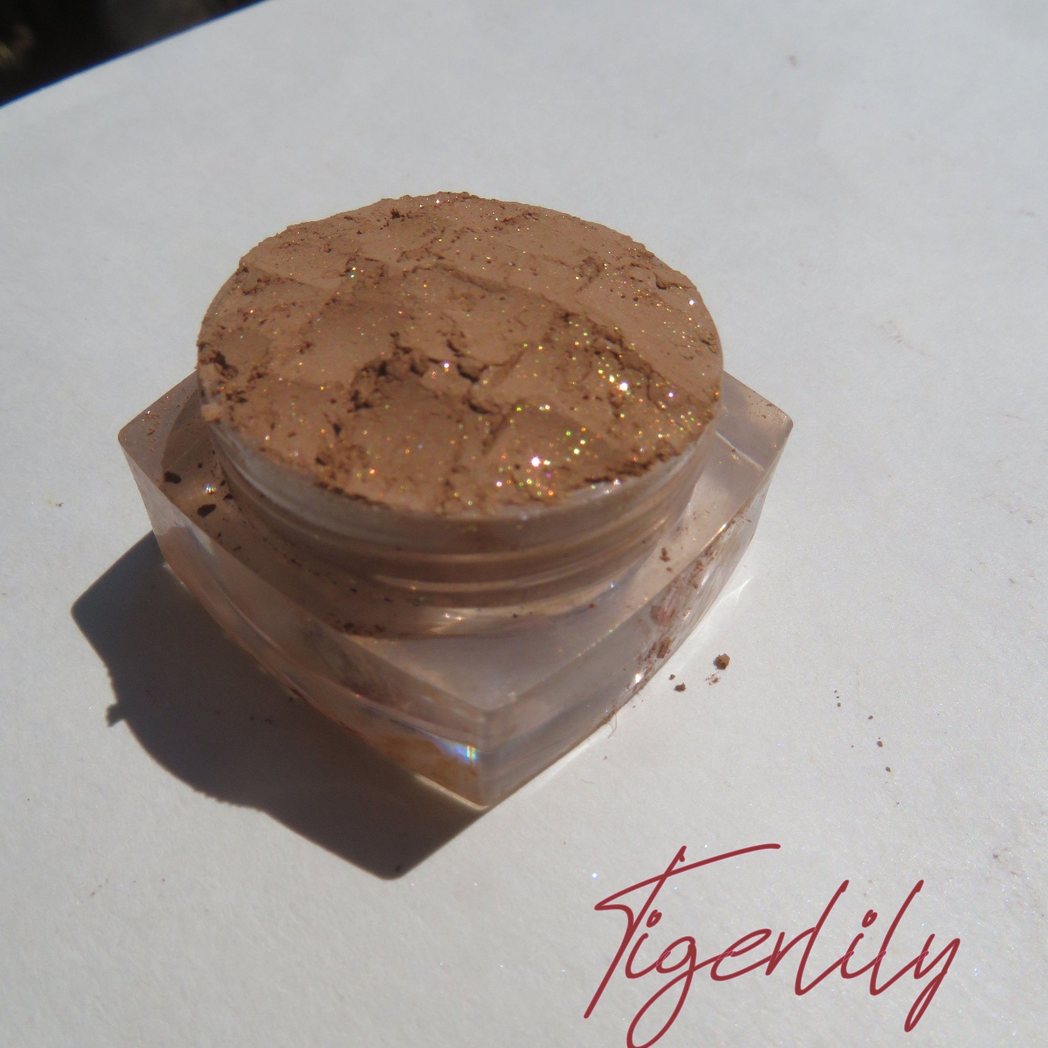 Side view of golden brown loose powder eyeshadow shimmering in sunlight with vegan cruelty-free label visible