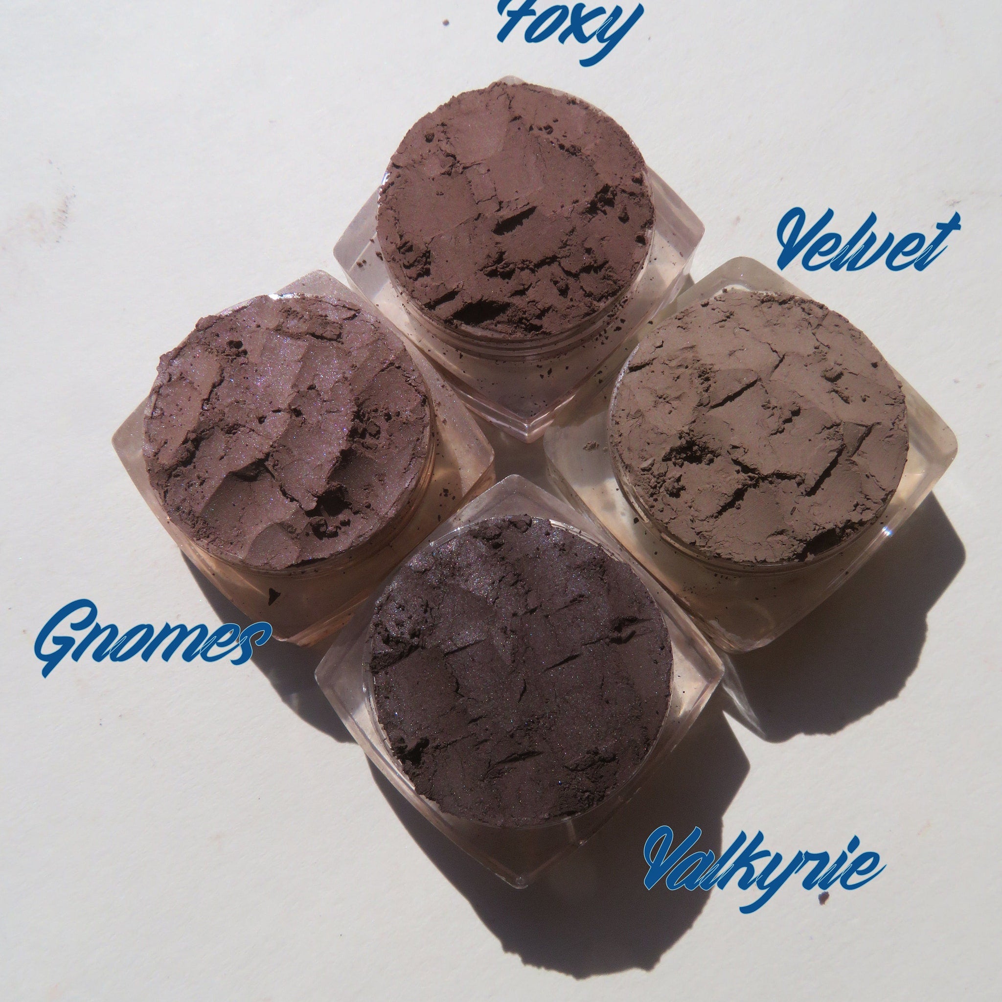 Four matte brown vegan loose mineral eyeshadows in round jars with black lids, arranged neatly on a white surface.