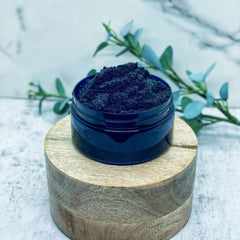 Body scrub in a dark blue jar with black granules, on a wooden pedestal with foliage